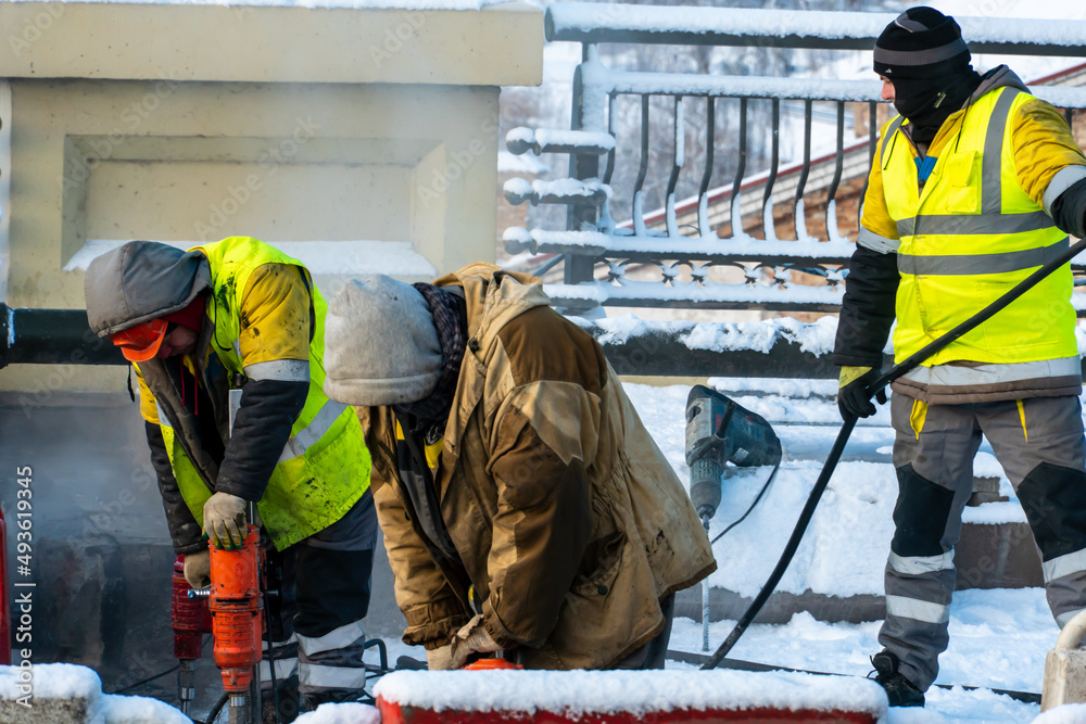 Employees of the road service in special yellow vests perform work on the repair of the roadway. Road repairs in difficult winter conditions during severe frost. Employees of the road service in special yellow vests perform work on the repair of the roadway. Road repairs in difficult winter conditions during severe frost.