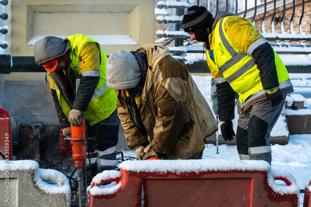 Employees of the road service in special yellow vests perform work on the repair of the roadway. Restoration of the deformation seam of the automobile bridge. Employees of the road service in special yellow vests perform work on the repair of the roadway. Restoration of the deformation seam of the automobile bridge.
