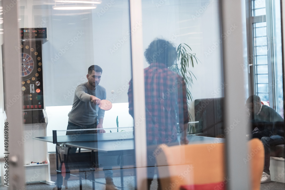 Two young start up business man playing ping pong tennis at modern creative office space people group have meeting and brainstorming in background