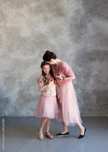 Mom and daughter in pink sweaters and pink skirts hold a heart-shaped cake in their hands