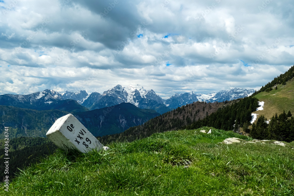 Border stone with scenic view in spring from Frauenkogel on mountain peaks in the Karawanks and Julian Alps, Carinthia, Austria. Border with Slovenia. Triglav National Park. Jesenice, Drava valley