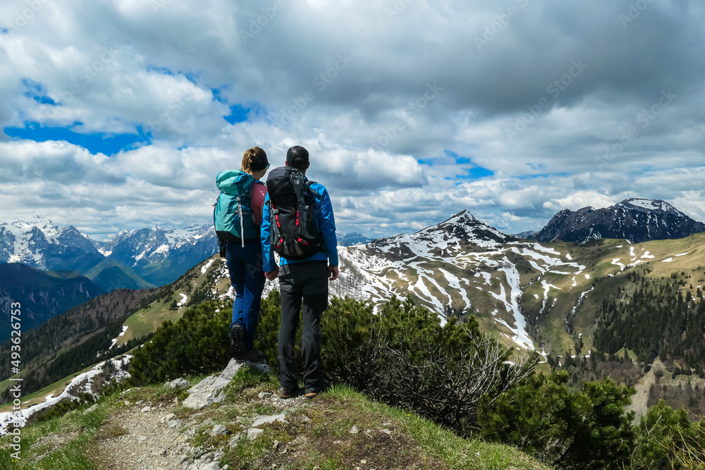 Active couple hiking on Frauenkogel with scenic view on mountain peaks in the Karawanks, Carinthia, Austria. Border with Slovenia. Triglav National Park. Kahlkogel (Golica). Snow melting in spring