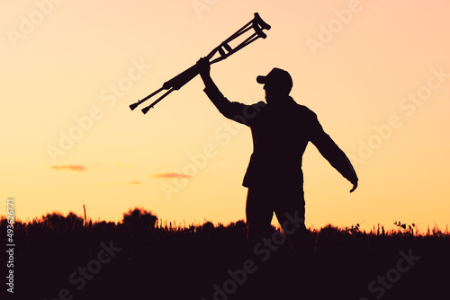 silhouette of a man on the background of the sunset holding crutches in his hand