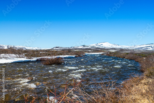 Spring scenery in the Dovrefjell, Norway, with creek, rocks, hills, mountains, and patches of snow