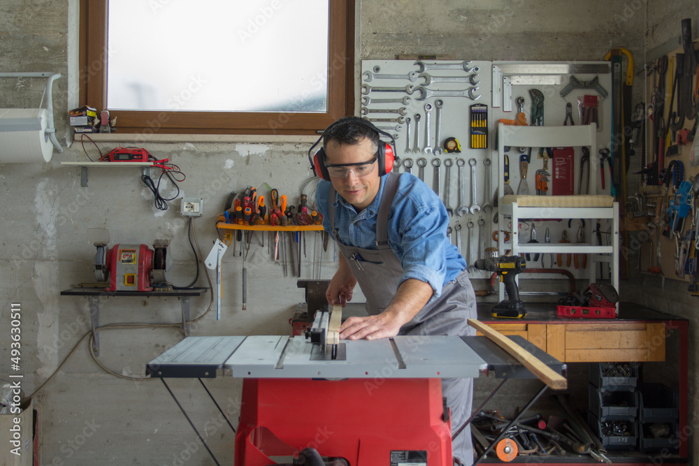 Handyman with individual safety devices while cutting pieces of wood with a bench saw. Home furniture restoration Handyman with individual safety devices while cutting pieces of wood with a bench saw. Home furniture restoration