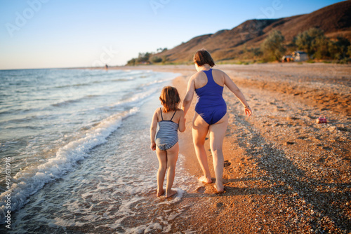 Cute european children run on the beach by the sea, happy childhood and freedom. Plus size kid, overweight, sisters play together