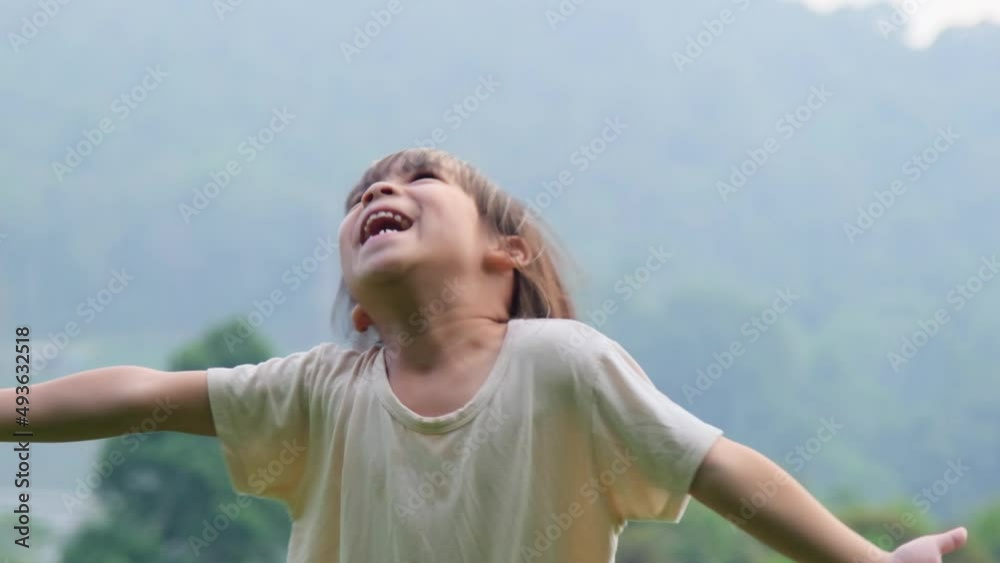 Cute little girl having fun catching rain drops. Kids play in summer rain. Child playing outdoor on rainy day.