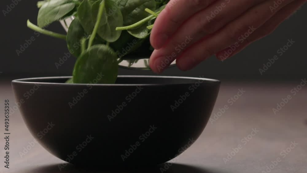 Slow motion man hand put spinach leaves in black bowl Slow motion man hand put spinach leaves in black bowl