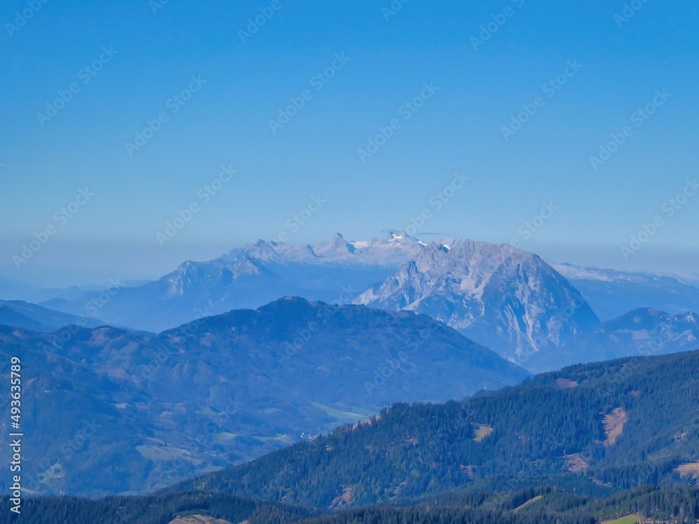 A panoramic view on a massive, stony Alps from Kaiserau Kreuzkogel region in Austria. There are endless mountains chains in the back. The slopes are overgrown with moss and grass. Sunny and bright day