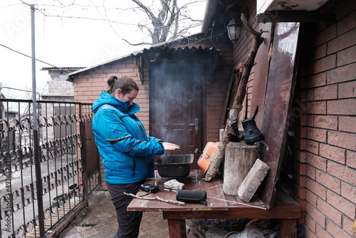 Mariupol, Ukraine - March 5, 2022: Woman warm up around a bonfire outside home under bombardment of the Mariupol City, Ukraine. photo