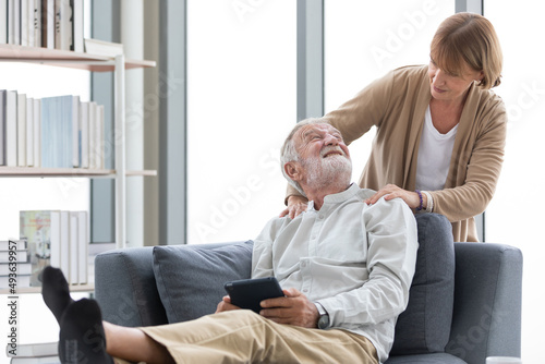 senior woman giving a shoulder massage to her husband on sofa