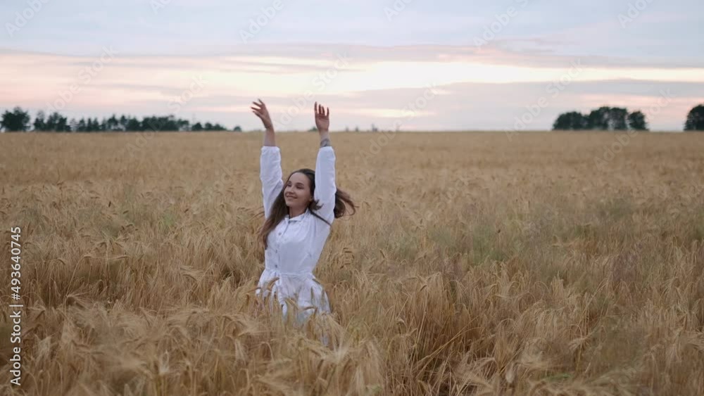 A young girl happily walking in slow motion through a field touching with hand wheat ears. Beautiful carefree woman enjoying nature and sunlight in wheat field at incredible colorful sunset A young girl happily walking in slow motion through a field touching with hand wheat ears. Beautiful carefree woman enjoying nature and sunlight in wheat field at incredible colorful sunset