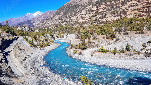 A panoramic view on river in Himalayan valley seen from Annapurna Circuit Trek, Nepal. Turquoise color of the river, big stones popping out of the river. Green forest around. Idyllic landscape. photo