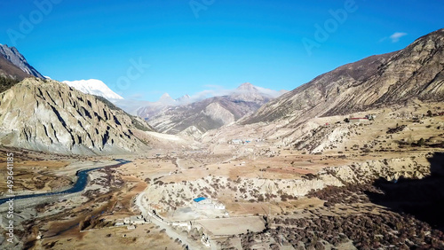 Way to Upper Pisang, Annapurna Circuit Trek, Nepal. Clear sky above the peak. Picturesque landscape, river in the bottom on the valley, small trees on the shores. White Himalayas mountain peaks
