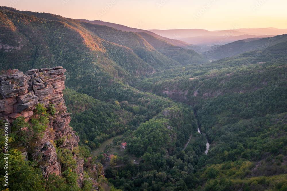 Obraz premium Golden hour view of a river canyon with hills covered by forests lighten by golden light and impressive vertical cliff in the foreground 1