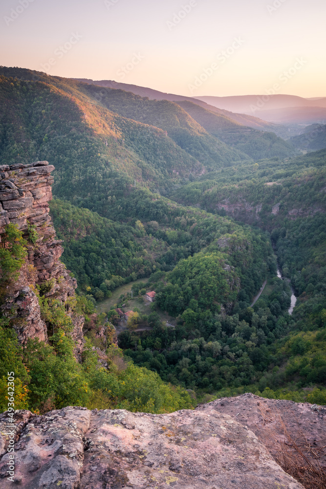 Golden hour view of a river canyon with hills covered by forests lighten by golden light and impressive vertical cliff in the foreground 1