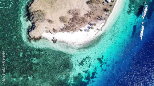Top down drone shot of paradise island in Komodo National Park, Flores, Indonesia. The island has scarcely any plants and is surrounded with idyllic white sand beaches. Few boats anchored on the shore