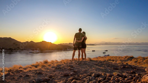 A couple standing and hugging on top of a small island  enjoying the morning sun over Komodo National Park  Flores  Indonesia. Golden hour over the islands and sea. They are enjoying their time. Love