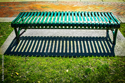 Green metal park bench on concrete slab by brick sidewalk with dramatic shadow