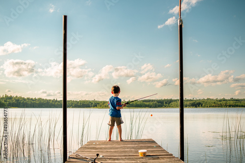 A young boy in a life jacket holds a fishing pole at the end of a dock in northern Minnesota