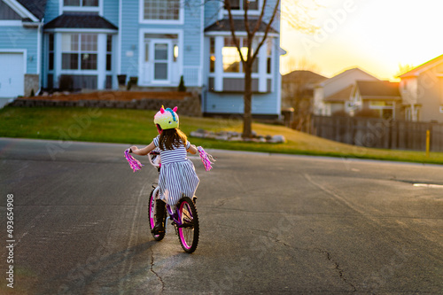 A girl in a unicorn helmet rides a bike with pink tassels at sunset