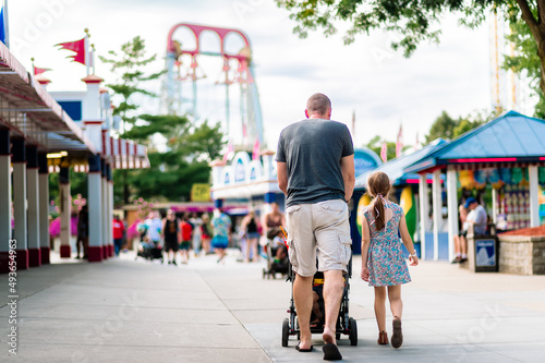 A father pushing a stroller and a daughter in a dress walk up the midway of an amusement park photo
