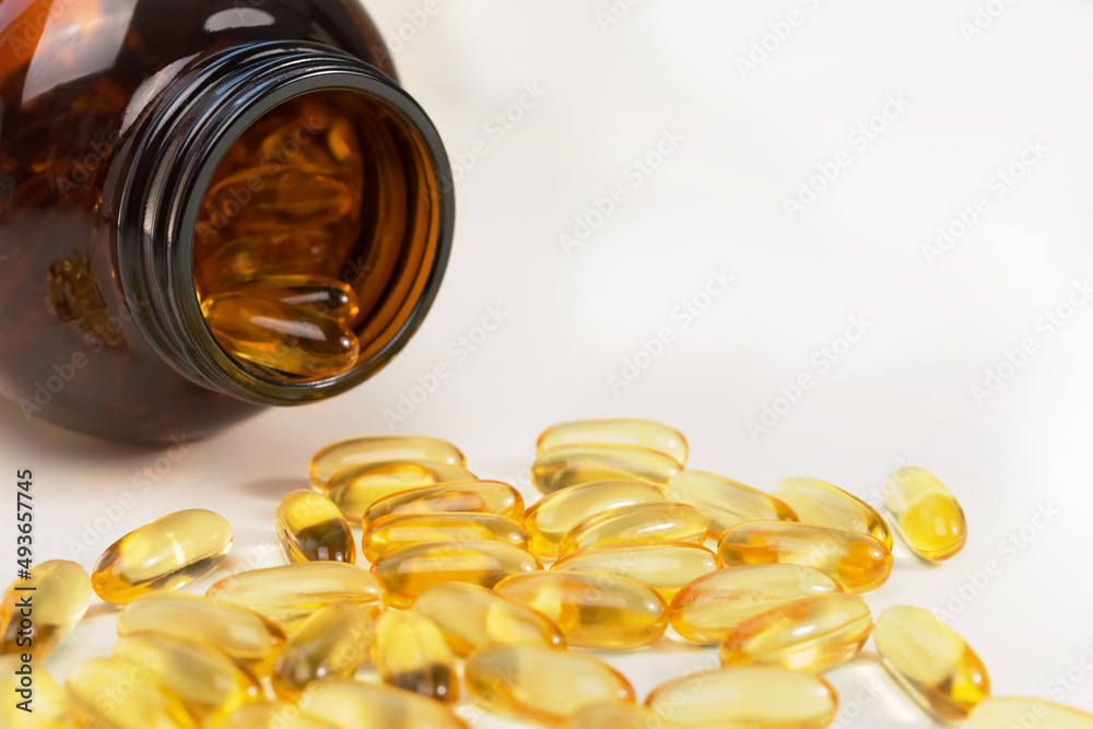 Dark glass jar for soft gel capsules Omega 3, scattered on white background. Copy space for text, close up, side view. Health care concept. Fish oil pills and supplements for health, sports, immunity. Dark glass jar for soft gel capsules Omega 3, scattered on white background. Copy space for text, close up, side view. Health care concept. Fish oil pills and supplements for health, sports, immunity.