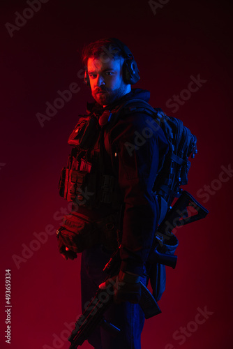 soldier. a man in military uniform with a weapon on a red background. blue-red colored light. war concept. in defense of the world. armed conflict