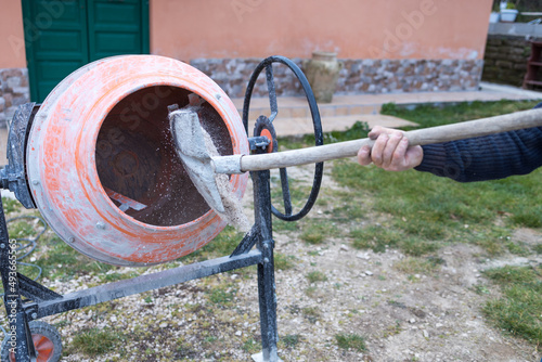 Man busy doing masonry work, mixing concrete with an electric cement mixer, wheelbarrow and shovel. bonus 110%, superbonus.