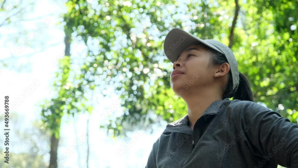 Tired Asian female athlete resting after jogging and looking at smartwatch in a green park on a sunny day. Fitness and lifestyle concept. Tired Asian female athlete resting after jogging and looking at smartwatch in a green park on a sunny day. Fitness and lifestyle concept.