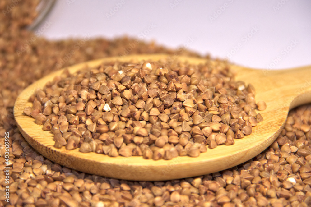 Buckwheat is scattered and in a wooden spatula. Lower angle. Close up. Buckwheat is scattered and in a wooden spatula. Lower angle. Close up.