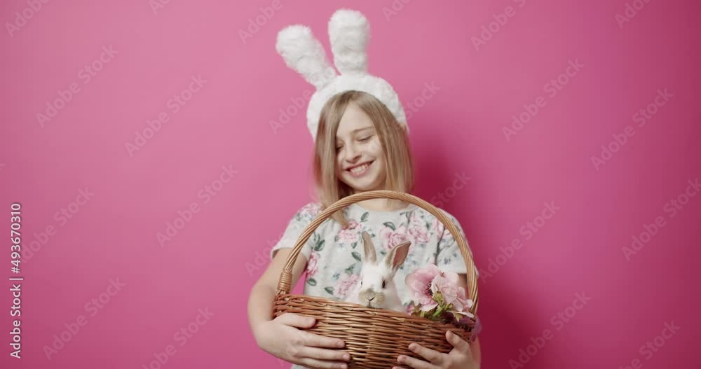 Cute teenage girl with rabbit ears poses and looks at the rooms with a basket of colored eggs and natural rabbit on an isolated pink background. Happy Easter. Adorable animal cute and fluffy rabbit. Cute teenage girl with rabbit ears poses and looks at the rooms with a basket of colored eggs and natural rabbit on an isolated pink background. Happy Easter. Adorable animal cute and fluffy rabbit.