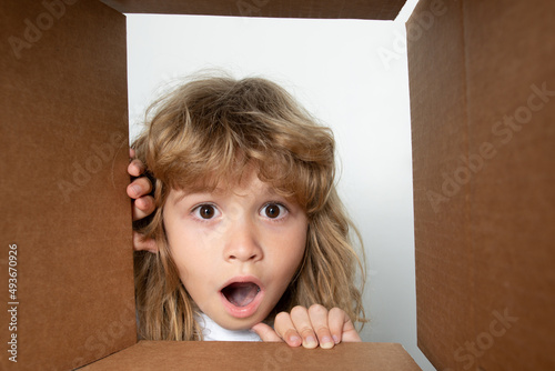 Happy little child boy is opening gift and looking inside cardboard box. Open box and delivery parcel for children.