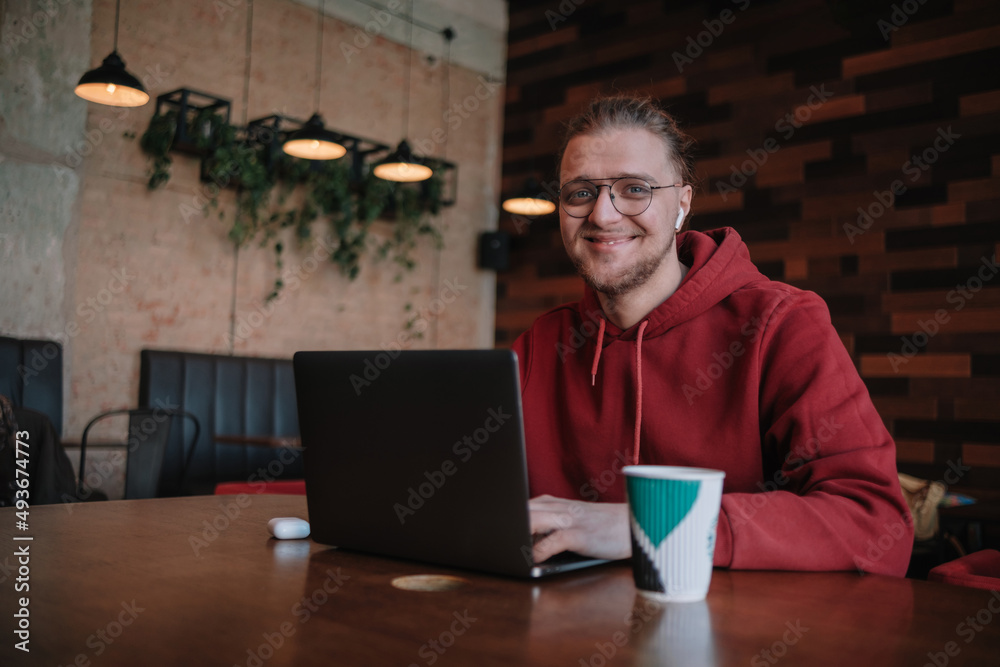 Portrait of happy male freelancer in optical eyewear for vision correction smiling at camera during break from web working online, cheerful hipster blogger sitting in cafe with mockup laptop Portrait of happy male freelancer in optical eyewear for vision correction smiling at camera during break from web working online, cheerful hipster blogger sitting in cafe with mockup laptop