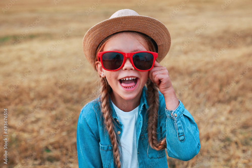 funny little girl with pigtails in sunglasses and straw hat outdoor in summer day. Summertime