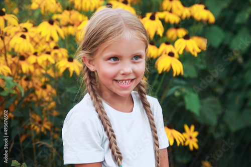 Close-up portrait of funny little girl with pigtails in yellow flowers in garden outdoor. Summertime