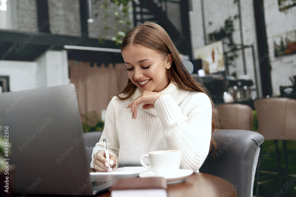 Beautiful young woman in casual clothing using laptop and smiling while working.Remote work