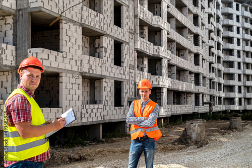 one worker stands with a tablet and the other stands further away from him at the new building