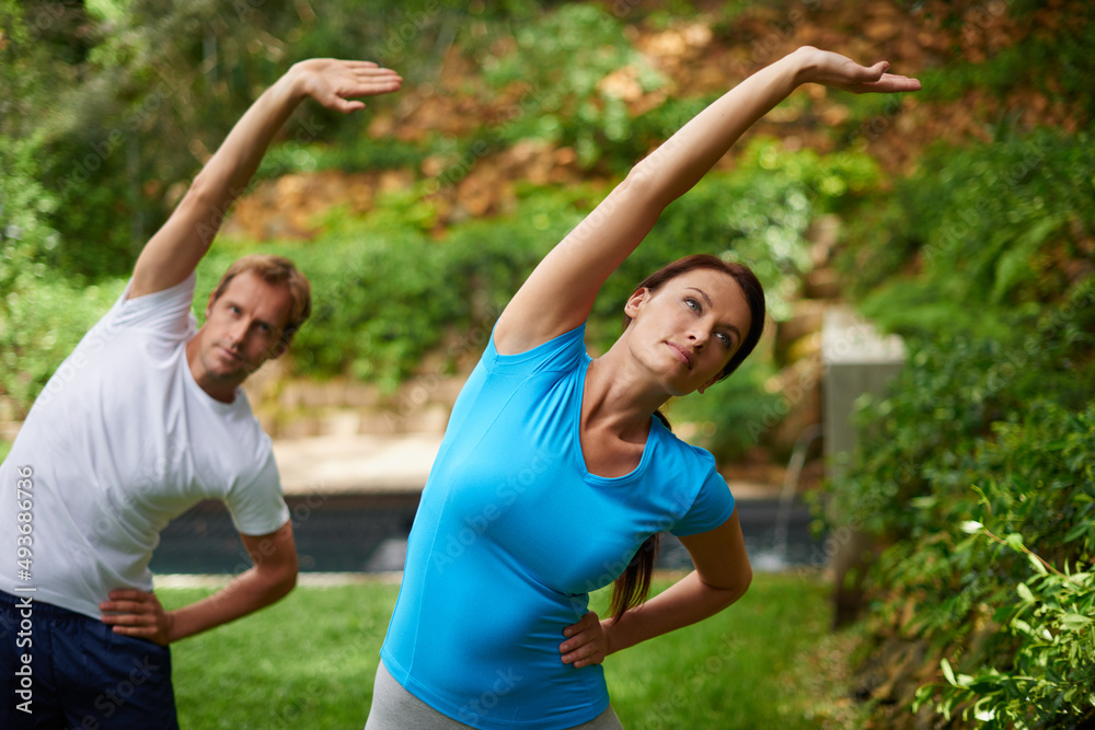 The path to flexibility. Shot of a man and woman performing a side stretch in an outdoor yoga class. The path to flexibility. Shot of a man and woman performing a side stretch in an outdoor yoga class.