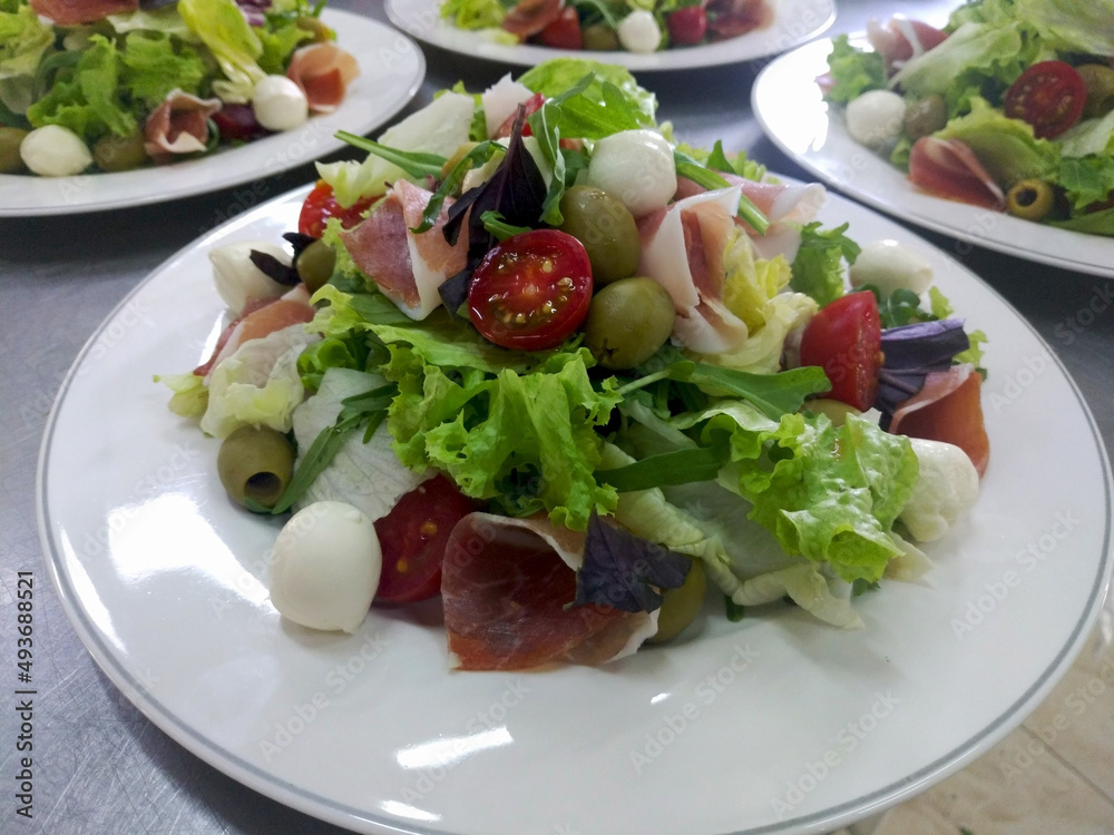 Mediterranean Kitchen. Fresh dietary salad with arugula, mozzarella, prosciutto and cherry tomatoes on a white plate. tasty and healthy food