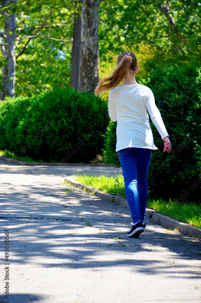 a girl runs along an asphalt path in a city park. spending time outdoors and being active in sports a girl runs along an asphalt path in a city park. spending time outdoors and being active in sports