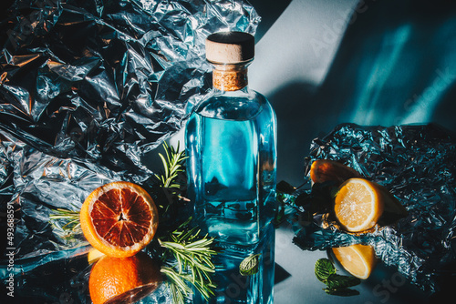 bottle of gin with lemon and grapefruit, rosemary, mint. Foil background