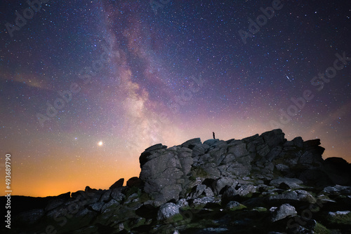 Silhouette of figure stargazing beneath the Milky Way and star filled sky, with planets and shooting stars visible