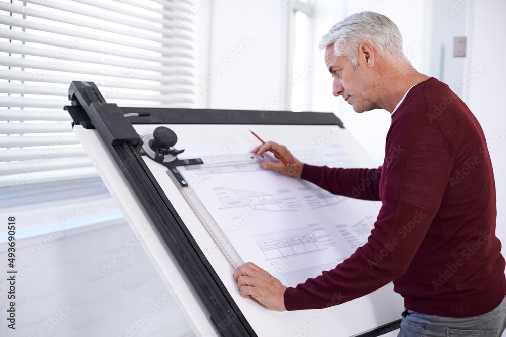 Doing what he does best. Cropped shot of a male architect working on a building plan at a drawing board. Doing what he does best. Cropped shot of a male architect working on a building plan at a drawing board.