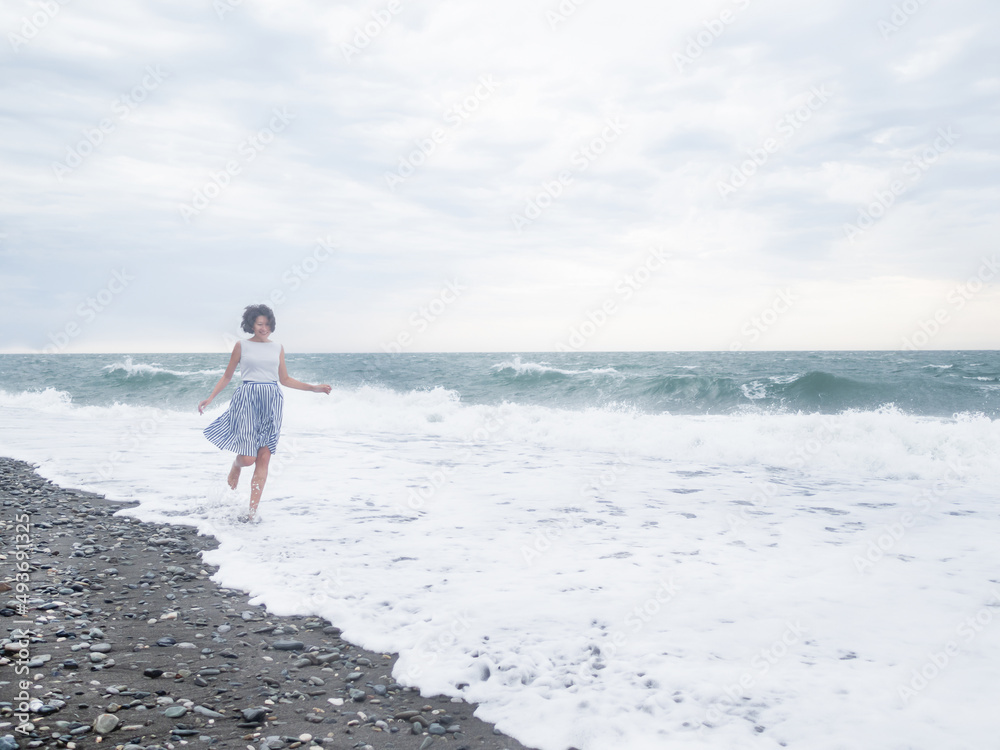 Happy woman is running on surf of stormy sea. Woman with hair ruffled with the wind. Wanderlust concept. Vacation on sea coast. Happy woman is running on surf of stormy sea. Woman with hair ruffled with the wind. Wanderlust concept. Vacation on sea coast.