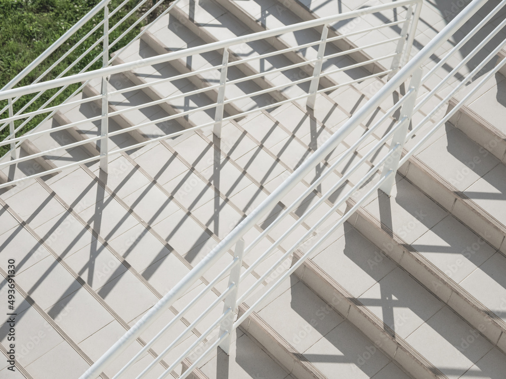 White exterior of outdoor staircase with railing. Sunlight and shadow on stone steps. Urban geometry. White exterior of outdoor staircase with railing. Sunlight and shadow on stone steps. Urban geometry.