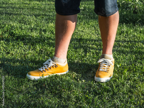 Man in bright yellow sneakers is standing on green grass lawn in park. Modern hipster's shoes. Urban fashion. © Konstantin Aksenov