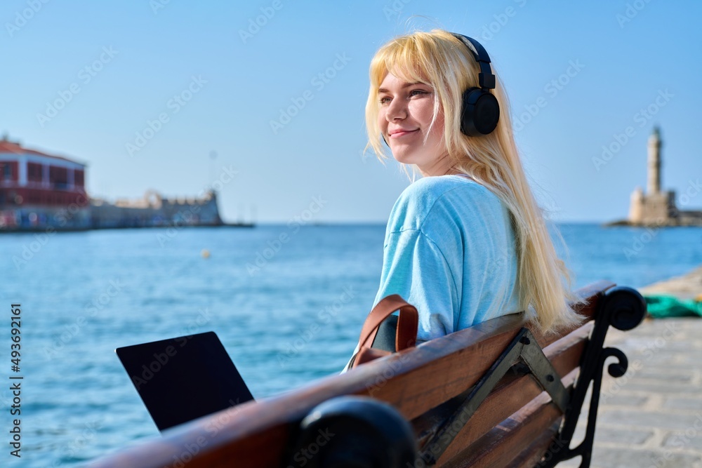 Young woman relaxing in headphones with a laptop on the seashore
