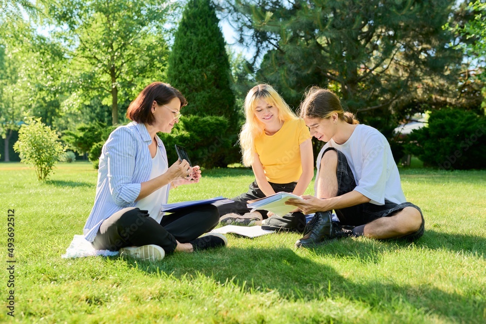 School teacher, psychologist, social worker talking to teenagers, sitting on grass School teacher, psychologist, social worker talking to teenagers, sitting on grass