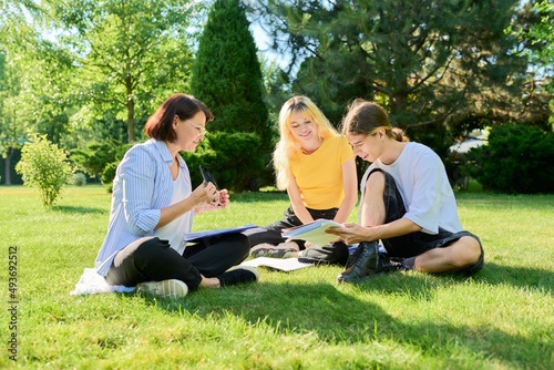 School teacher, psychologist, social worker talking to teenagers, sitting on grass © Valerii Honcharuk